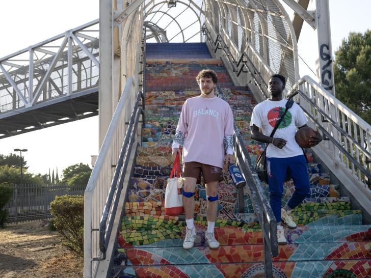 Jeremy and Kamal walk down the mosaic stairs of an overpass walkway carrying gym gear in the 2023 remake of White Men Can’t Jump